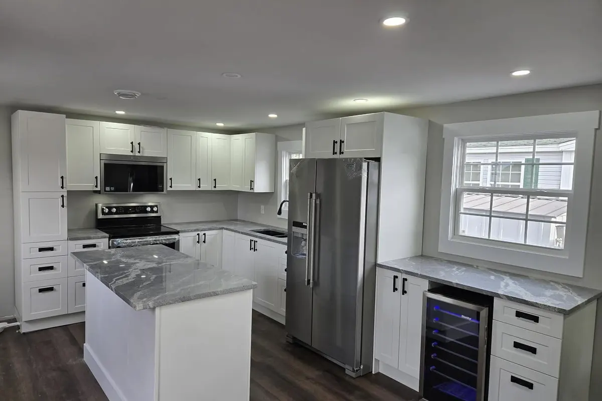 A finished kitchen: white shaker cabinets, grey stone counters, an island, a steel fridge and a wine fridge.