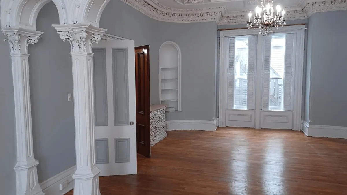 A restored room: white columns and arches, a plaster ceiling with a chandelier, and wood floors.